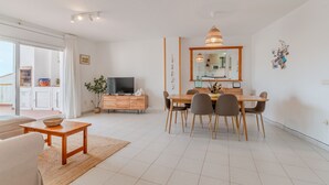 A modern living room with a dining area, a TV, and a large window. - Flateli Empuriabrava (Empuriabrava)