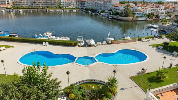 A marina with boats, a swimming pool, and a view of a coastal town with buildings. - Flateli Empuriabrava (Empuriabrava)