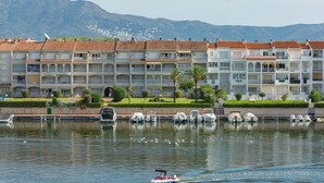 A waterfront hotel with multiple balconies, a marina with boats, and a mountainous backdrop. - Flateli Empuriabrava (Empuriabrava)