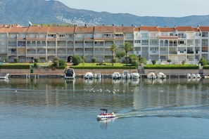 Um hotel à beira-mar com várias varandas, uma marina com barcos e montanhas ao fundo.