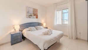 A neatly made bed with white linens and two pillows, a bedside table with a lamp, and a painting on the wall. - Flateli Empuriabrava (Empuriabrava)