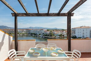 Uma varanda com mesa posta para refeições, com vista para um rio e uma cidade com edifícios e montanhas ao longe.