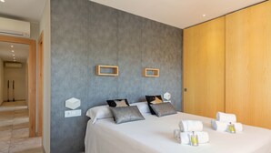 A modern hotel room with a large bed, grey textured wall, wooden paneling, and a hallway leading to another room. - Flateli l'Escala Vista Mar (L'Escala)