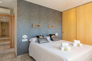 Ein modernes Hotelzimmer mit einem großen Bett, einer grauen Wand mit Struktur, Holzverkleidung und einem Flur, der zu einem anderen Zimmer führt.