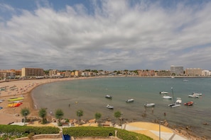 Ein Küstenstrand mit Booten, Sonnenschirmen und einer Uferpromenade.