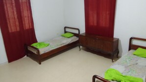 A small, sparsely furnished room with two single beds, a wooden dresser, and red curtains. - Dar Mourad (Djerba Midun, Médenine)