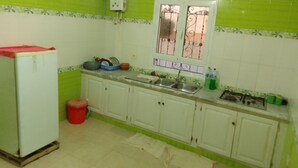 A kitchen with white cabinets, a sink, a stove, and a window with decorative bars. - Dar Mourad (Djerba Midun, Médenine)