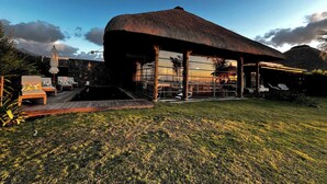 Una casa moderna con techo de paja, terraza de madera y mobiliario exterior.