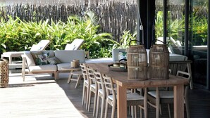 Un patio al aire libre con mesa y sillas de madera, rodeado de sillones y un sofá.