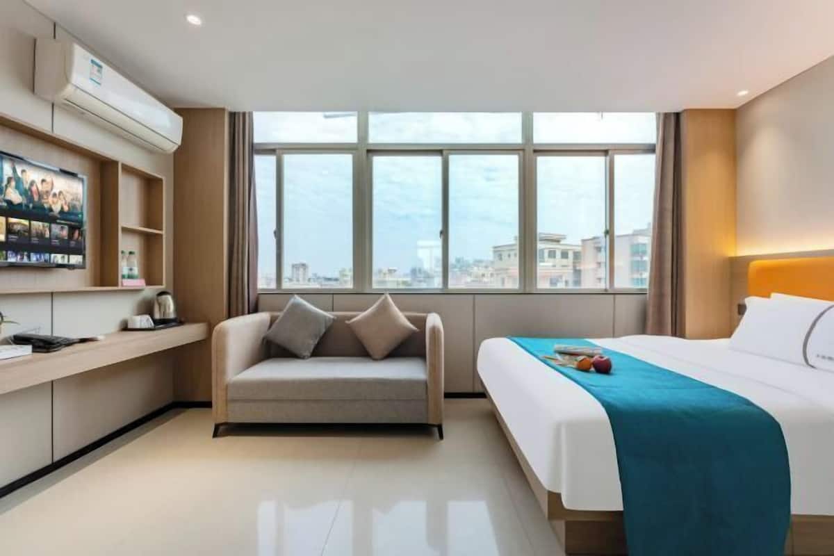 Una habitación de hotel con cama, sofá, televisión y un ventanal grande.