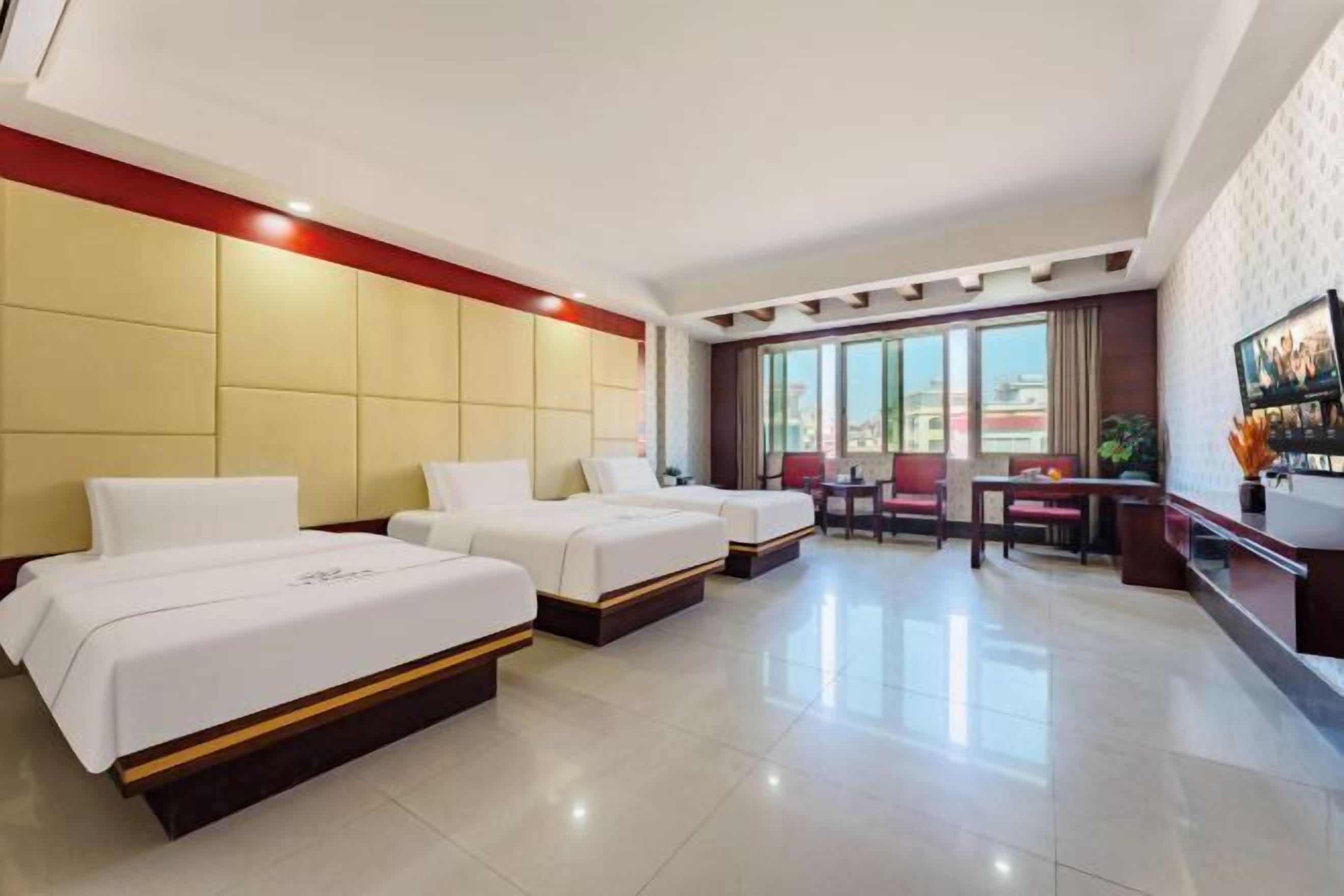 Habitación de hotel con tres camas, un escritorio, una silla y un ventanal grande.
