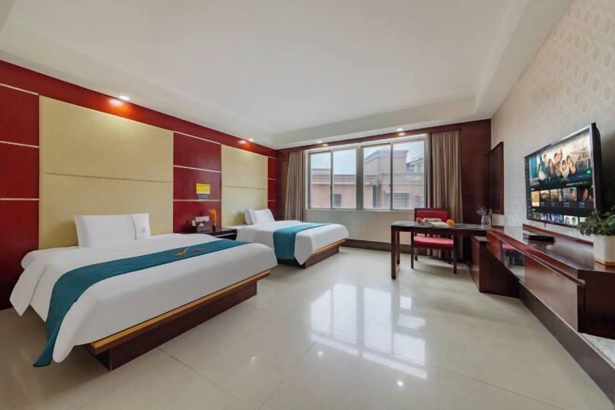 Habitación de hotel con dos camas, un escritorio, un televisor y una ventana con vistas.