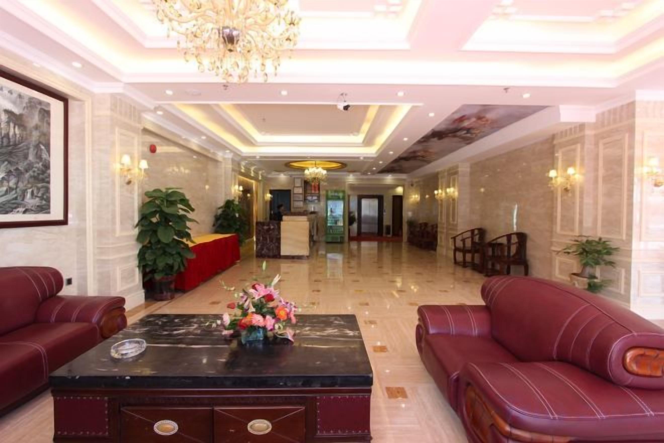 A hotel lobby with a reception desk, seating area, and a chandelier.