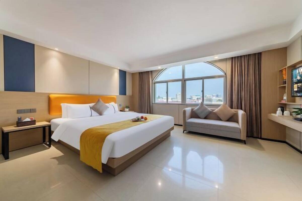 Habitación de hotel moderna con una cama grande, un sofá, un escritorio y un amplio ventanal con vistas a la ciudad.