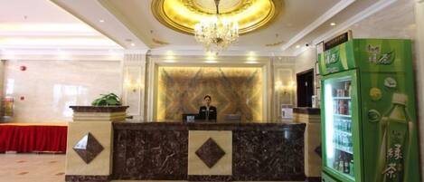 A hotel reception area with a marble counter, a chandelier, and a green beverage dispenser.