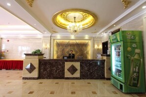 Área de recepção de hotel com balcão de mármore, lustre e dispensador de bebidas verde.