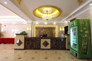 A hotel reception area with a marble counter, a chandelier, and a green beverage dispenser.