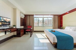 A hotel room with a bed, a desk, a chair, a TV, and a window with curtains.