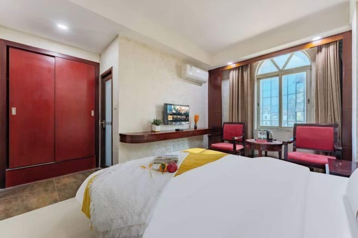 Habitación de hotel con cama, escritorio y silla, televisor y ventana con cortinas.