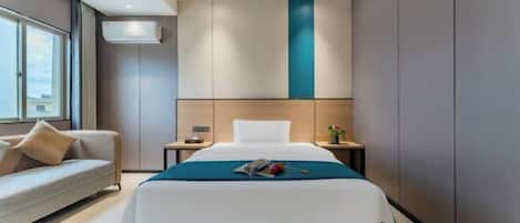A modern hotel room with a large bed, a sofa, a nightstand, and a window with curtains.