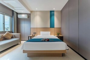 A modern hotel room with a large bed, a sofa, a nightstand, and a window with curtains.
