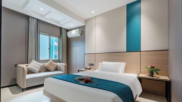 A modern hotel room with a large bed, a sofa, a nightstand, and a window. - Q+ Maoming Daxi Holiday Hotel (Maoming)