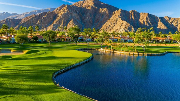 A golf course with a water hazard, surrounded by houses and mountains.