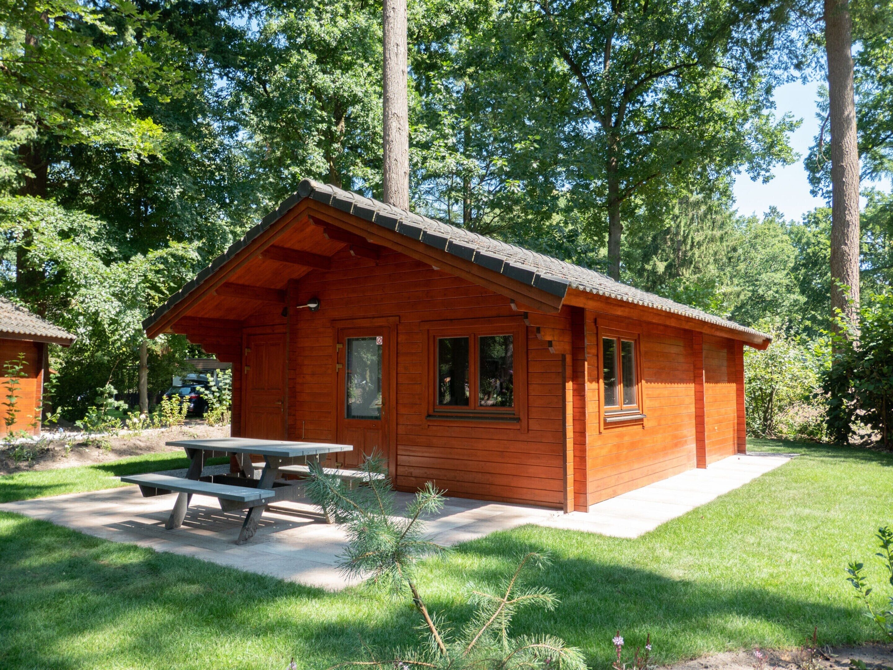 A wooden cabin with a covered patio, a picnic table, and a small garden area.