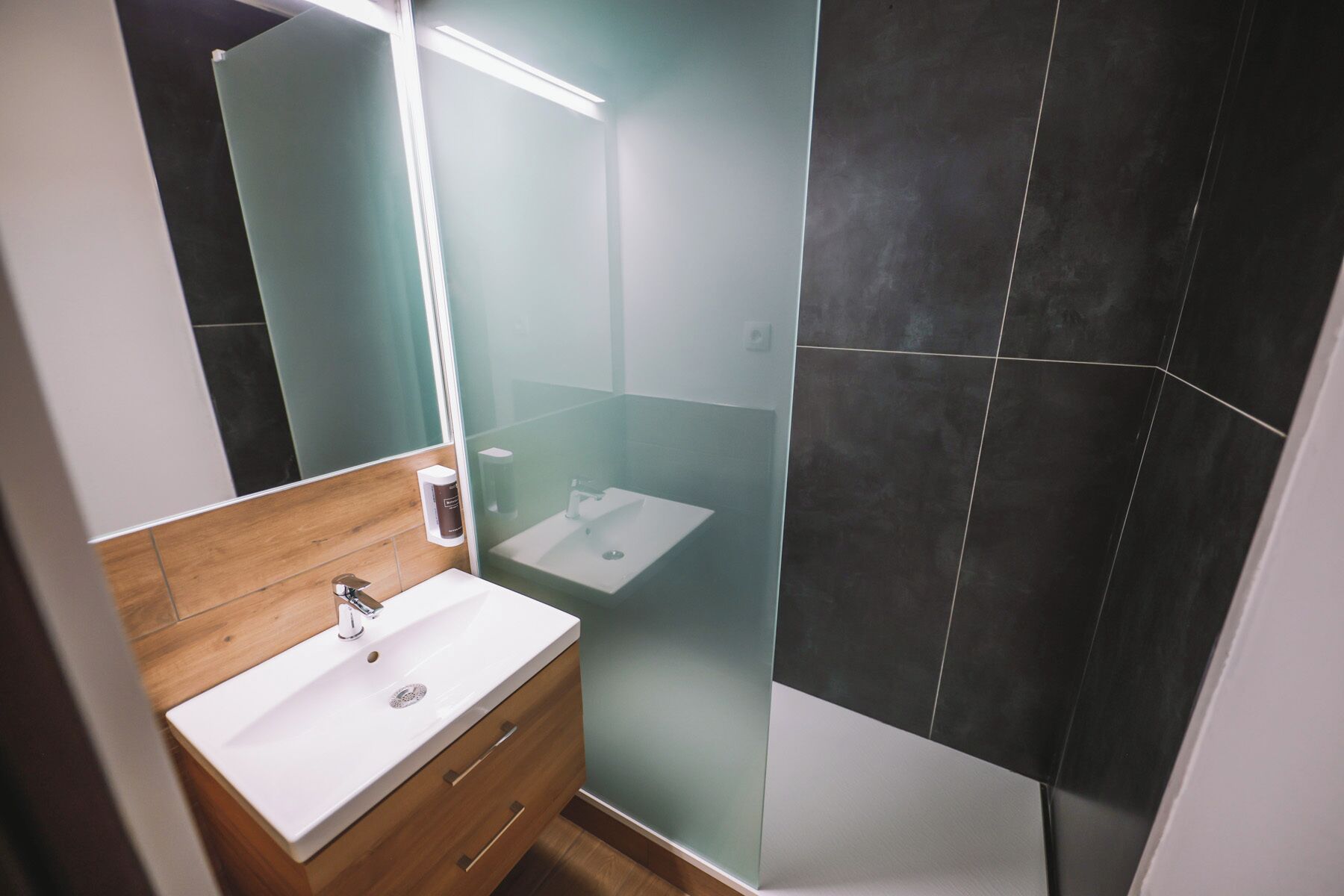 A modern bathroom with a white sink, wooden vanity, and a mirror.