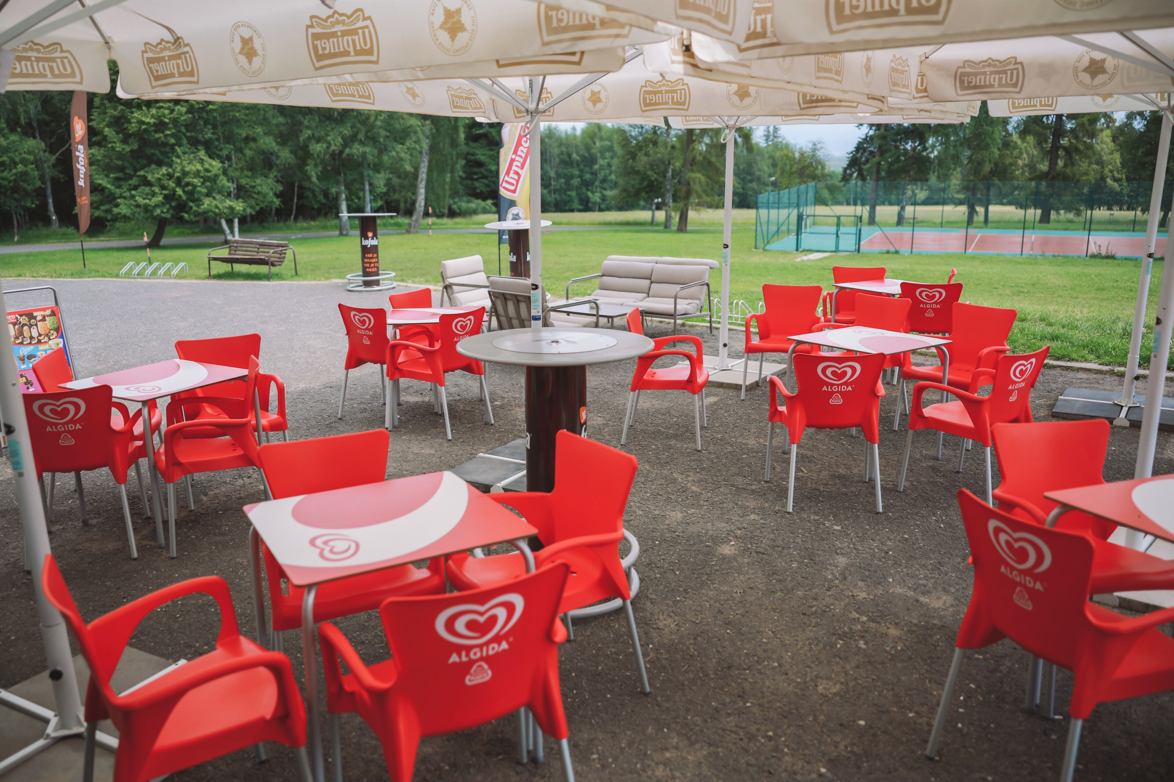 An outdoor seating area with red chairs and tables, umbrellas, and a view of a park.