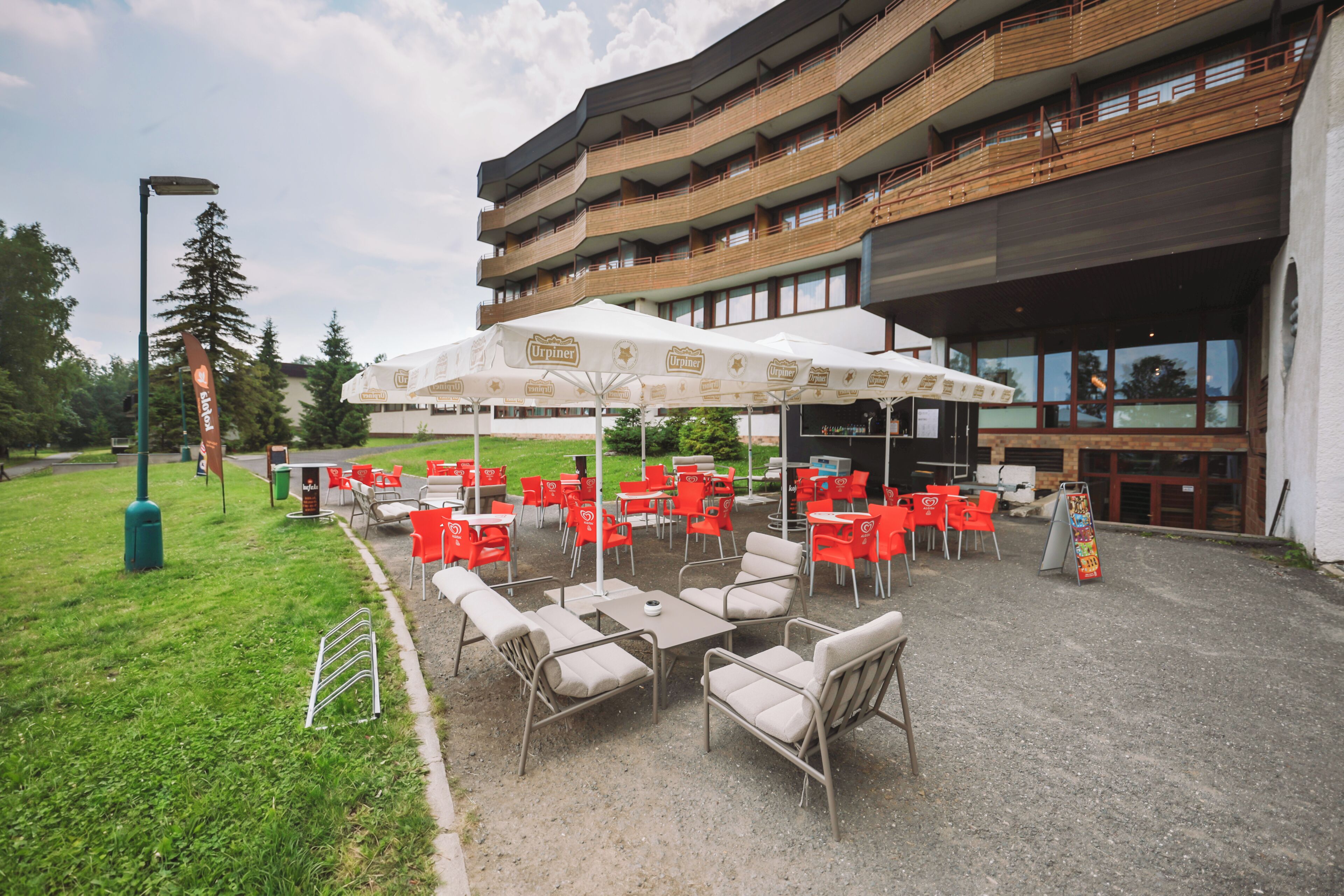 Een terras met tafels en stoelen, een overdeeld gedeelte met parasols, en een gebouw met meerdere balkons op de achtergrond.