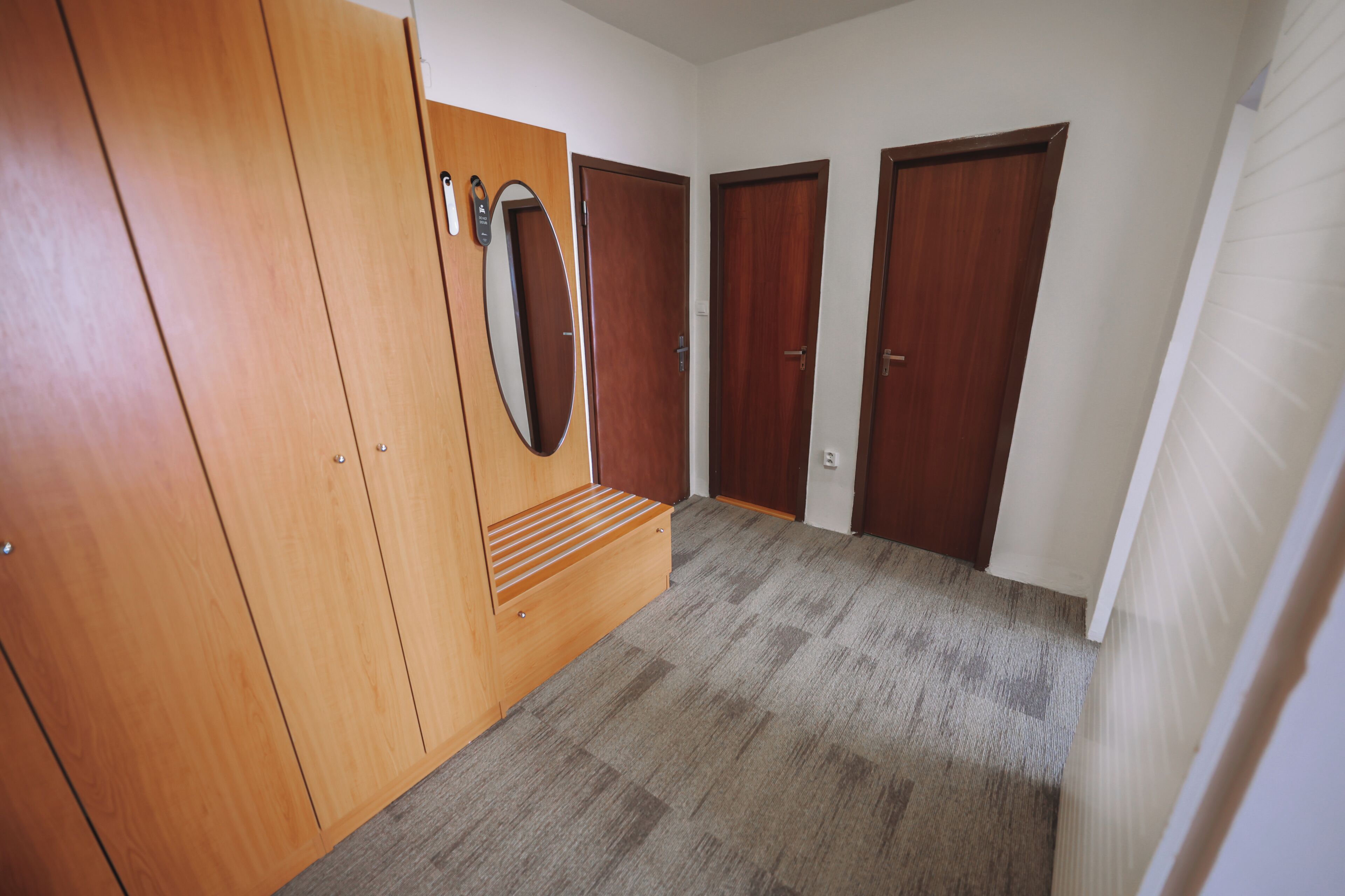 Un couloir avec une armoire en bois, un miroir et trois portes en bois.