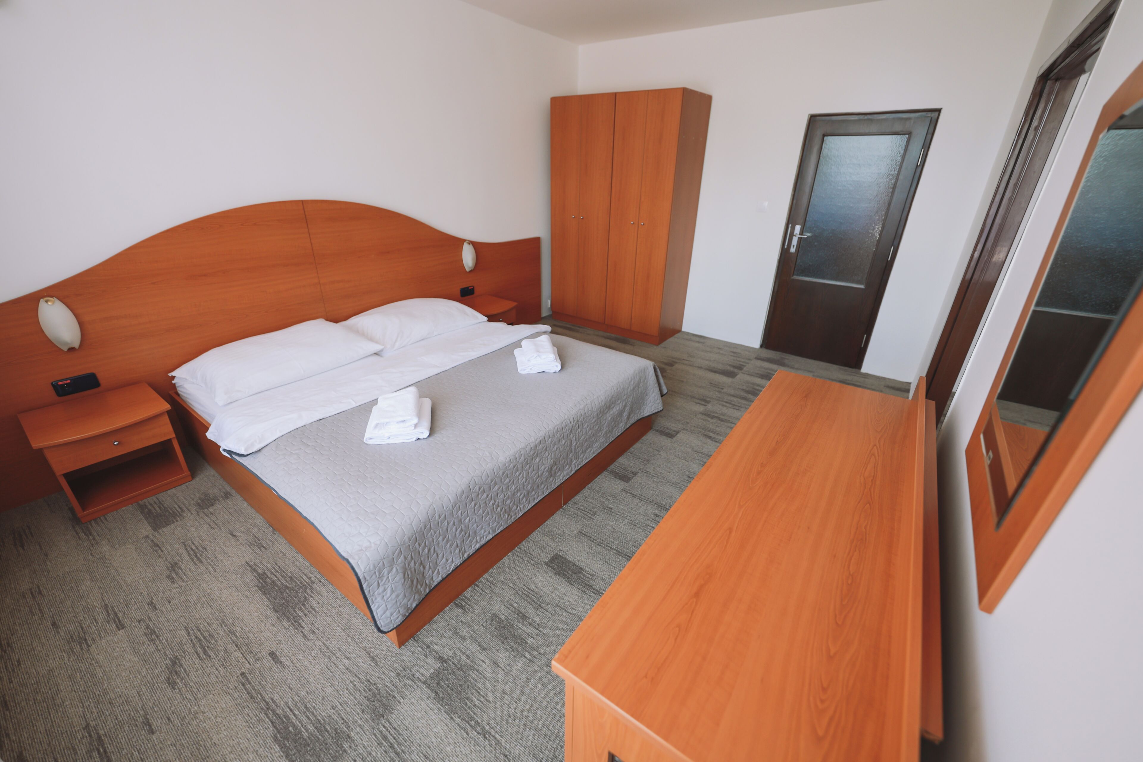 Ein Hotelzimmer mit Bett, Holzschrank, Nachttisch und Spiegel.