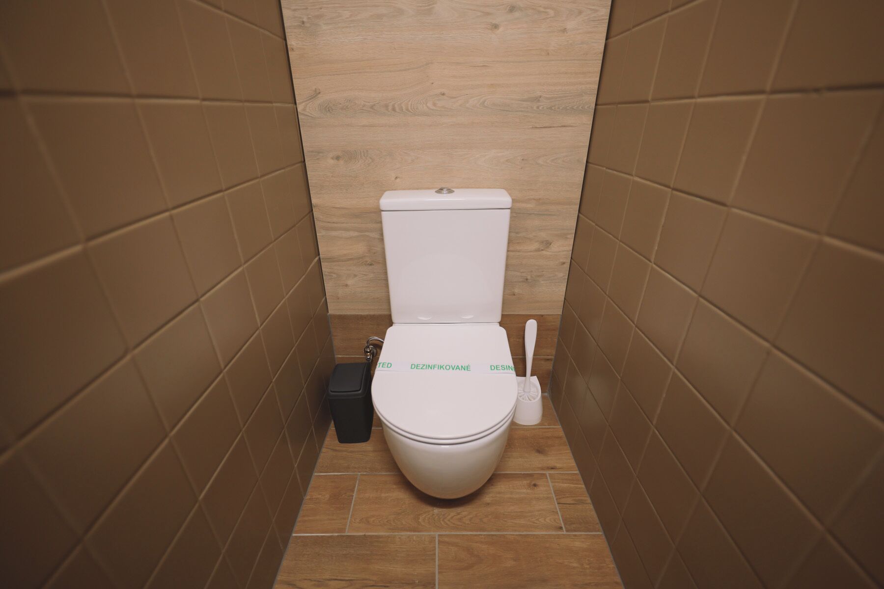 A small, narrow bathroom with a white toilet, a black trash bin, and a white bidet.