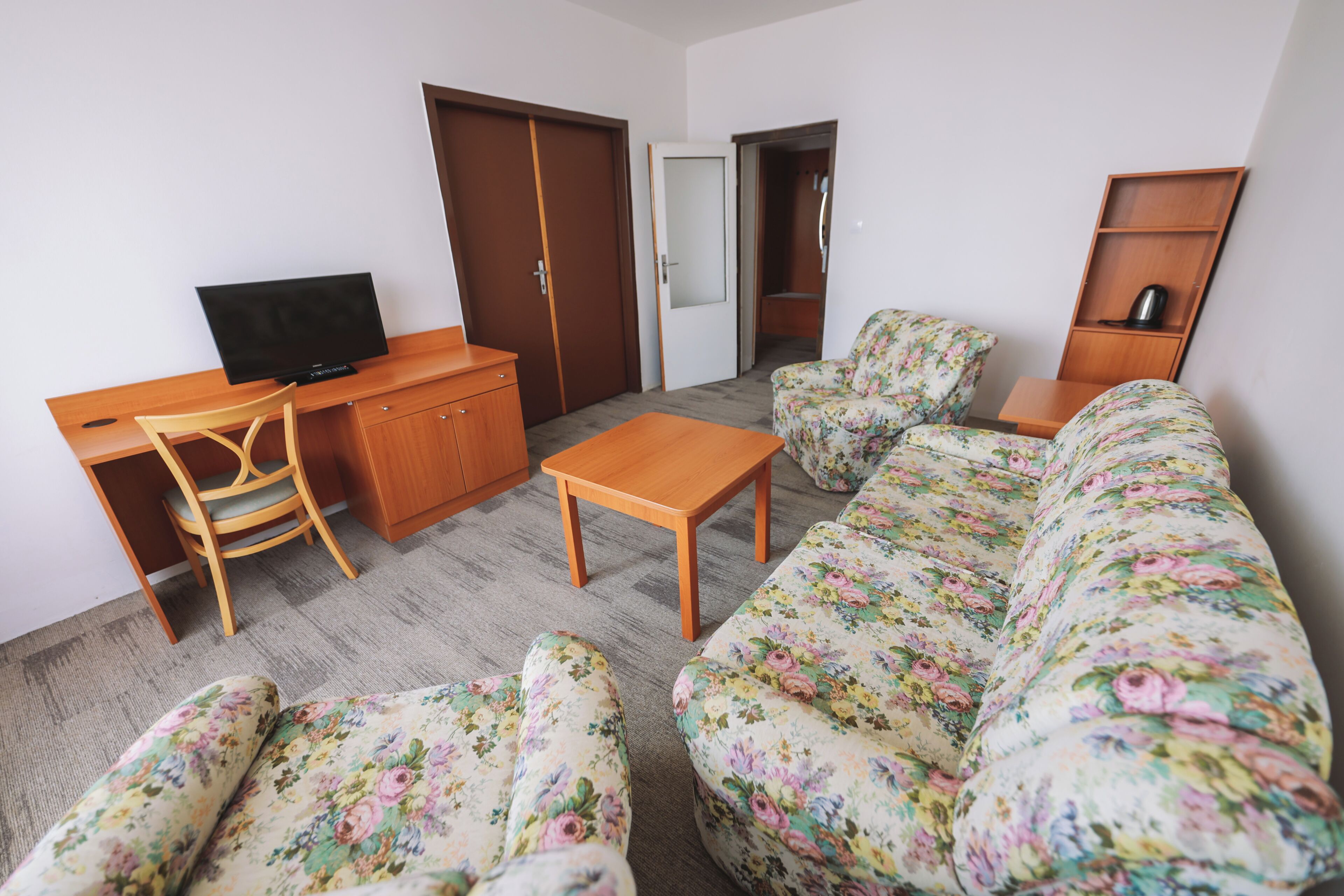 A living room with a sofa, a wooden coffee table, a TV on a desk, and a chair.