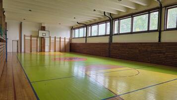 Una cancha de baloncesto interior con piso de madera, aro de baloncesto y pared de madera con ventanas.