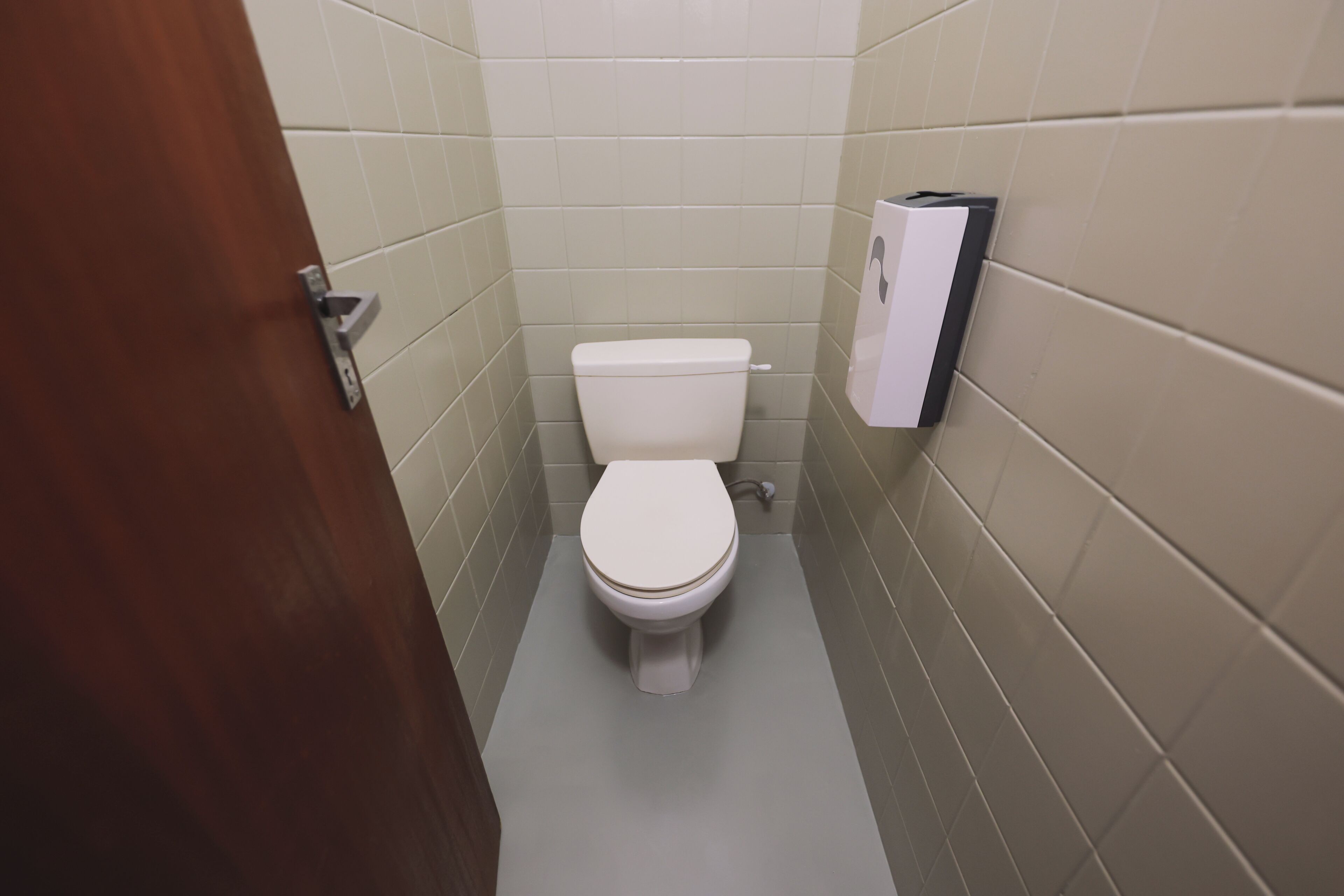 A small, narrow bathroom with a toilet, a hand dryer, and a door.