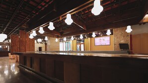 A bar area with a wooden counter, hanging pendant lights, and a television screen on the wall. - Atlas Hotel Tatry (Vysoké Tatry)
