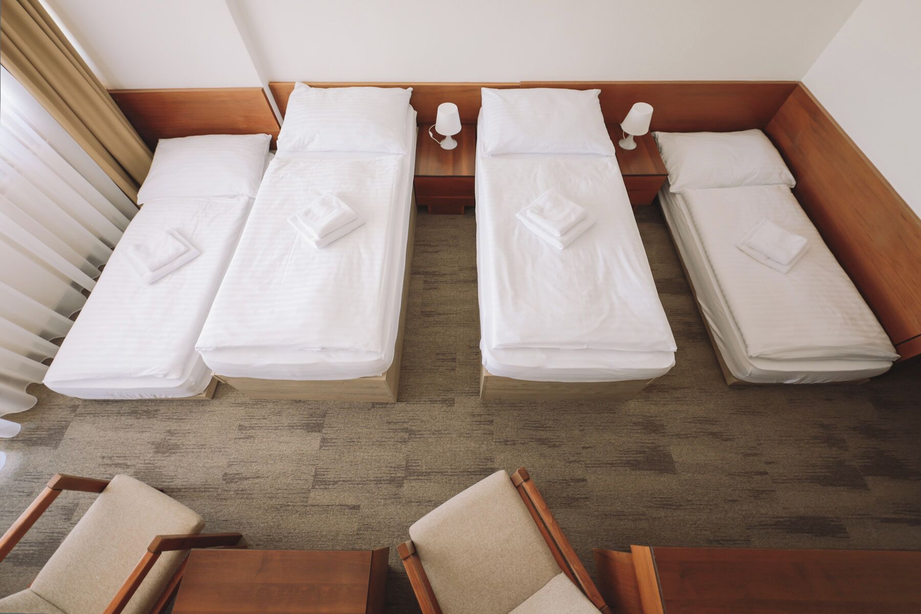 A hotel room with two single beds, a wooden headboard, a small table, and two chairs.