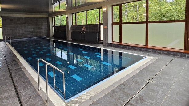 An indoor swimming pool with a tiled floor, safety railings, and large windows offering views of greenery. - Atlas Hotel Tatry (Vysoké Tatry)