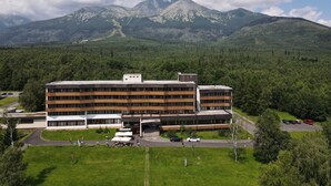 A modern hotel with a flat roof and multiple floors, surrounded by lush greenery and mountains in the background. - Atlas Hotel Tatry (Vysoké Tatry)