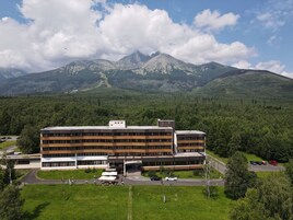 Un hotel moderno con techo plano y varios pisos, rodeado de abundante vegetación y montañas al fondo.