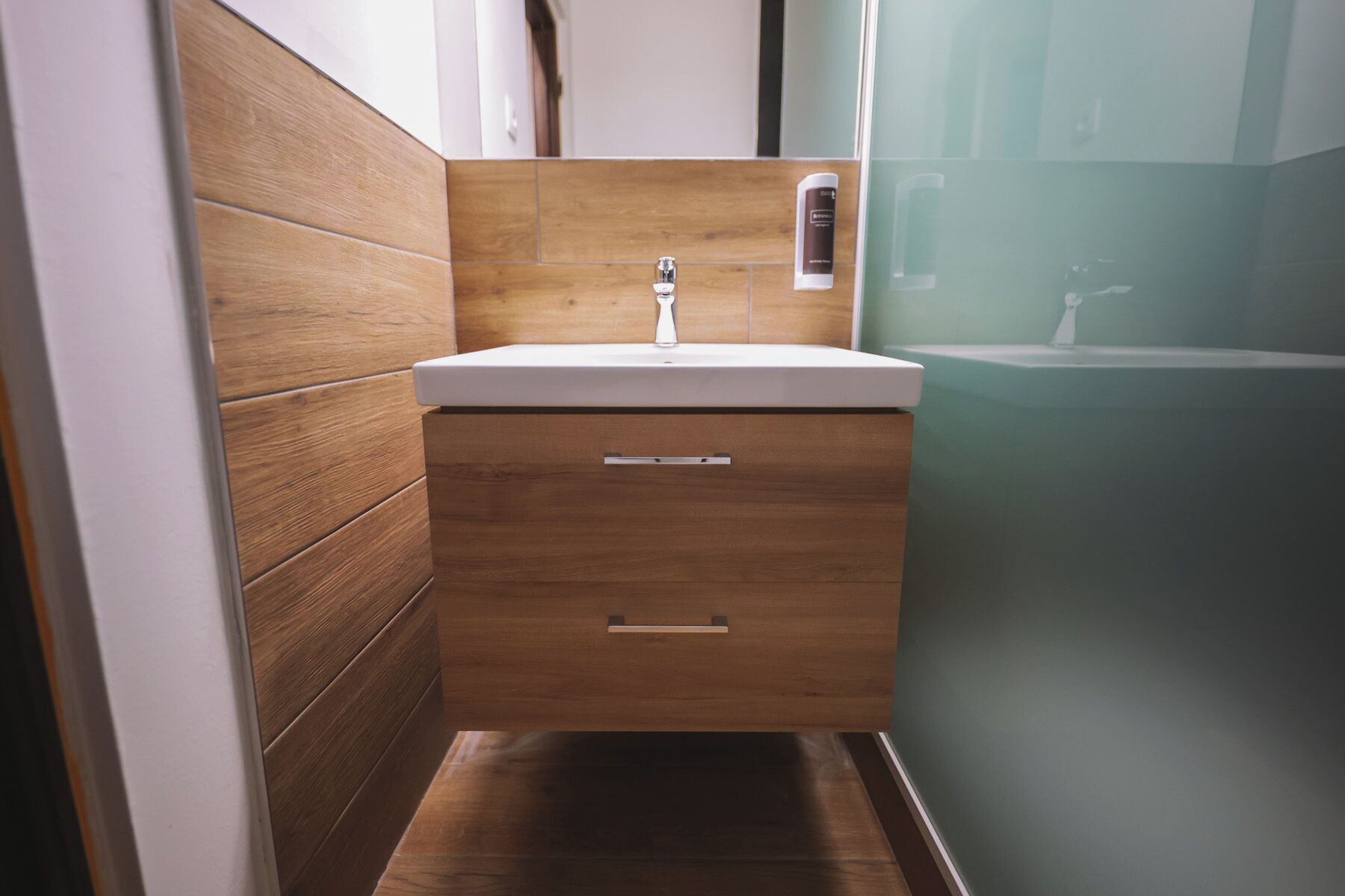 Un bany modern amb un lavabo de fusta, un rentapel obert i una cabina de dutxa de vidre.