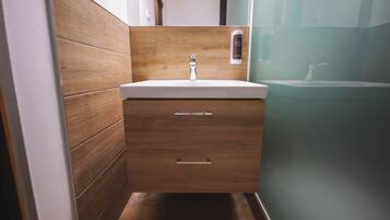 Un bany modern amb un lavabo de fusta, un rentapel obert i una cabina de dutxa de vidre.
