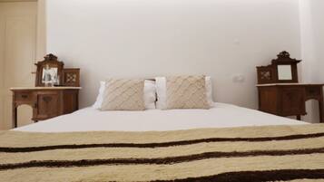 A bed with a striped rug, two bedside tables with clocks, and a mirror on the wall.