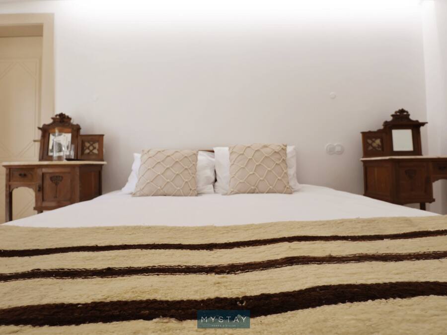 A bed with a striped rug, two bedside tables with clocks, and a mirror on the wall.