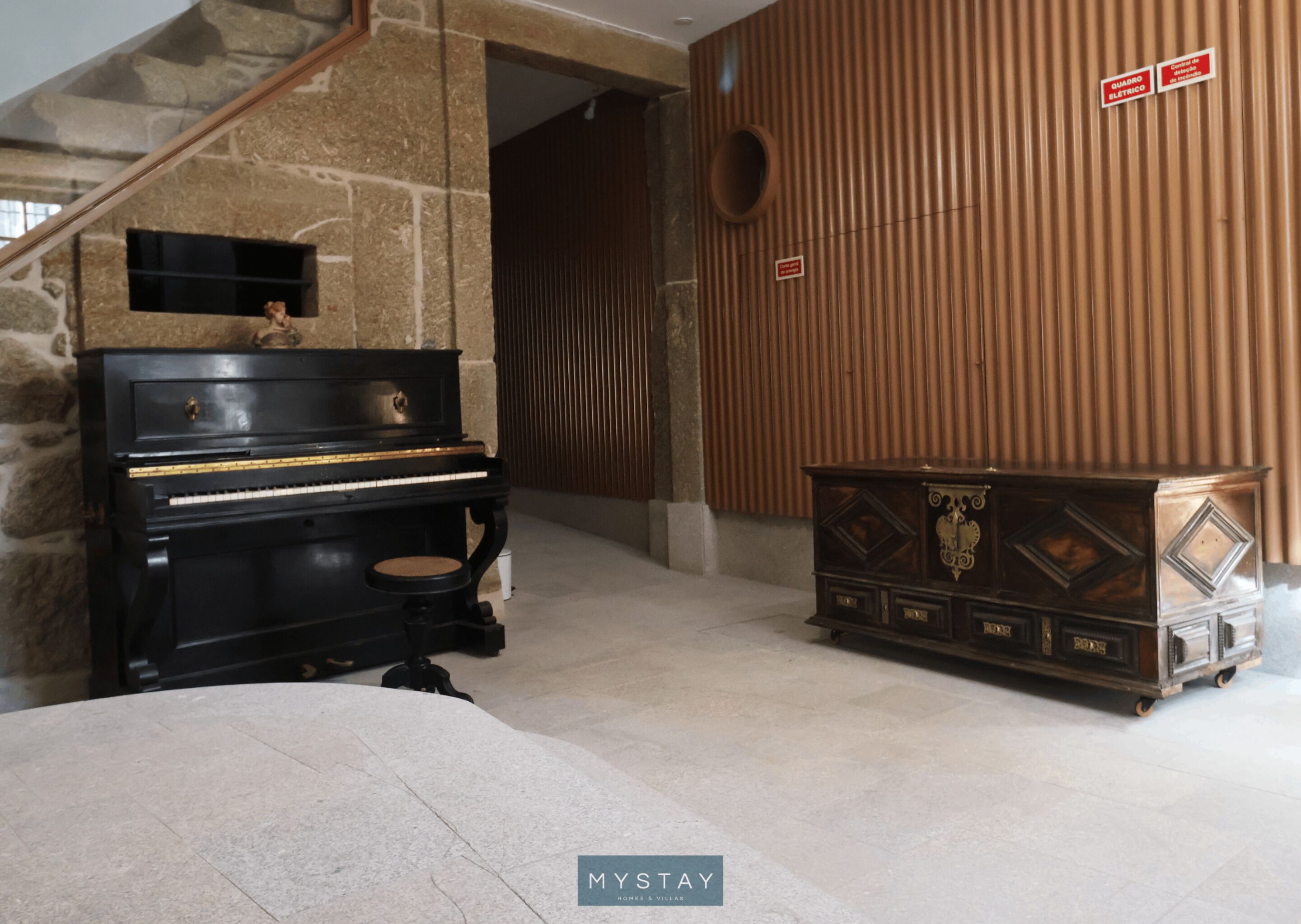 A room with a piano, a wooden cabinet, and a stone wall.
