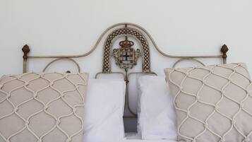Una cama con cabecera de metal, dos almohadas color beige con diseño de mosquitero y una almohada blanca.