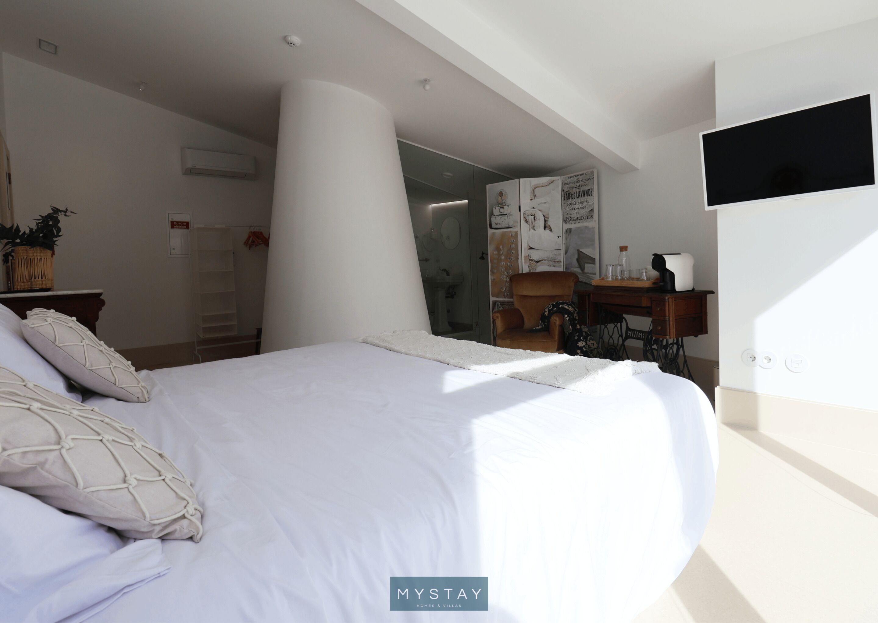 Ein Schlafzimmer mit einem großen Bett, einem an der Wand montierten Fernseher und Blick ins Zimmer durch eine Glastür.
