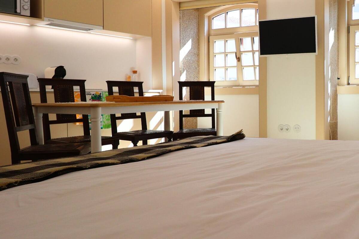A bedroom with a bed, a desk, chairs, and a television.